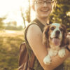 chica alegre con anteojos con su perro en brazos